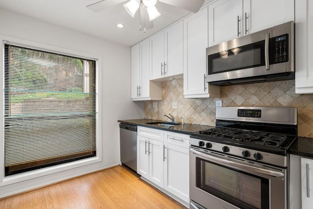 kitchen with sink, dark stone countertops, white cabinets, stainless steel appliances, and light wood-type flooring