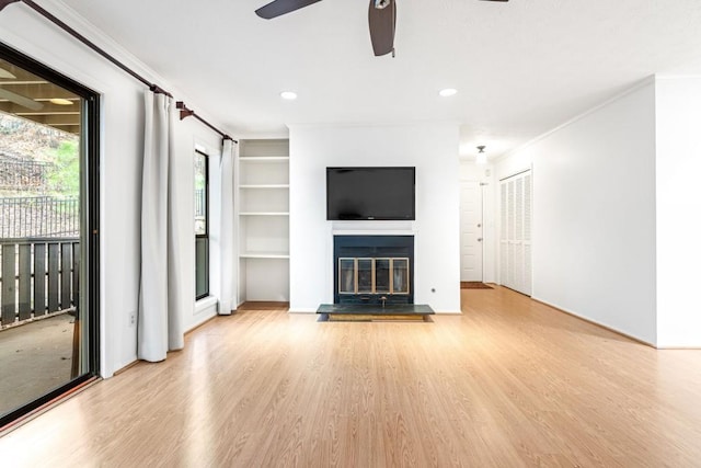 unfurnished living room with crown molding, ceiling fan, built in shelves, and light wood-type flooring