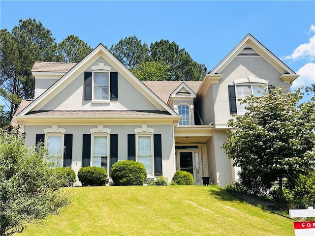 view of front of property featuring stucco siding, a front lawn, and a shingled roof