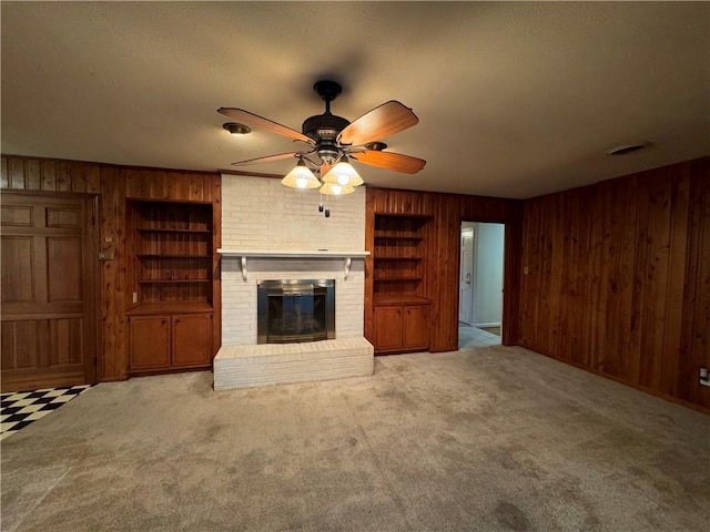 unfurnished living room featuring carpet, a fireplace, wooden walls, and built in shelves