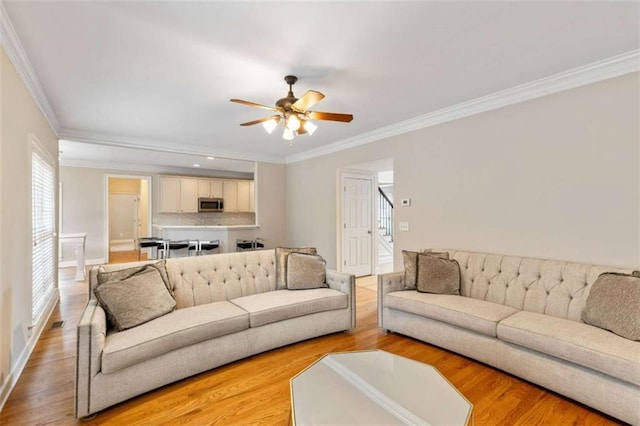 living area with stairs, a ceiling fan, wood finished floors, and ornamental molding