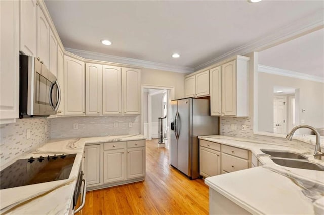 kitchen with light wood-style flooring, stainless steel appliances, crown molding, and a sink