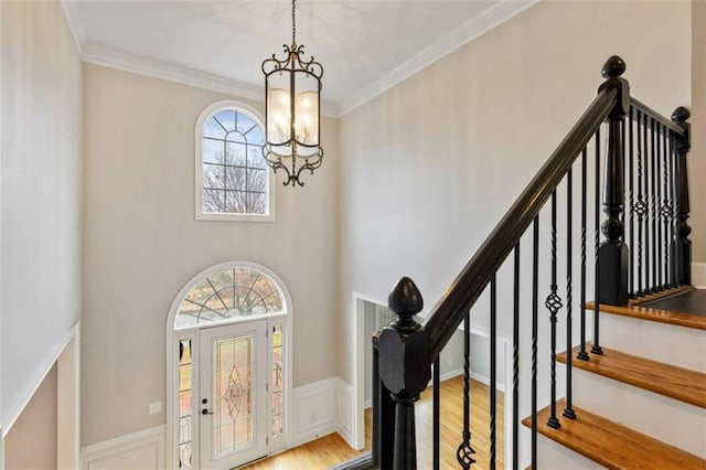 entrance foyer featuring crown molding, stairway, a wainscoted wall, an inviting chandelier, and wood finished floors