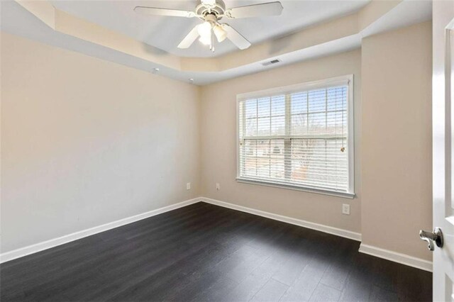 empty room featuring visible vents, baseboards, ceiling fan, dark wood-type flooring, and a raised ceiling