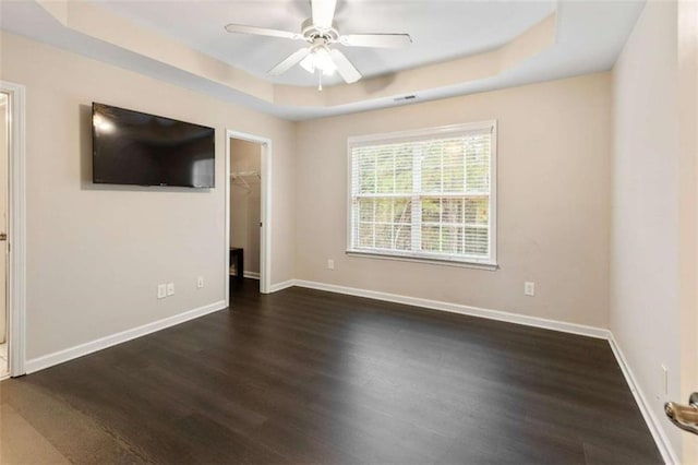 unfurnished room featuring ceiling fan, a tray ceiling, baseboards, and dark wood-style floors