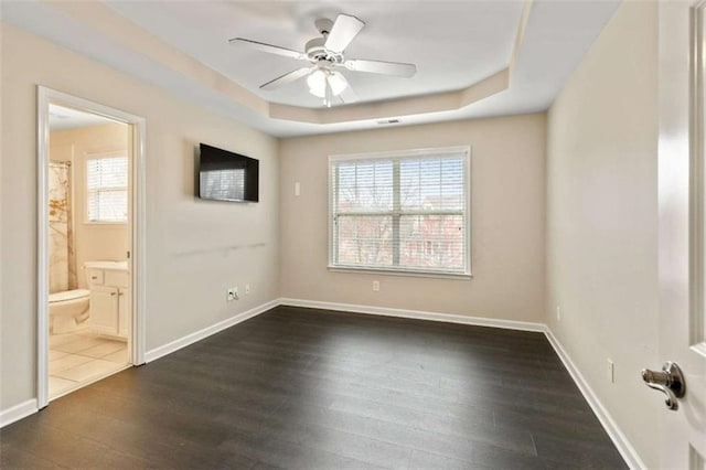 spare room with a tray ceiling, baseboards, dark wood-style floors, and a ceiling fan