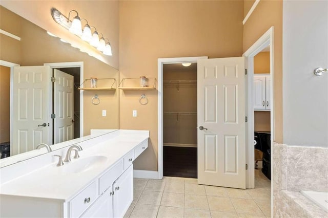 bathroom featuring vanity, baseboards, a tub, tile patterned flooring, and a spacious closet