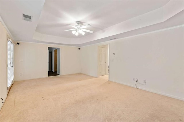 unfurnished room featuring a tray ceiling, visible vents, light colored carpet, and a ceiling fan