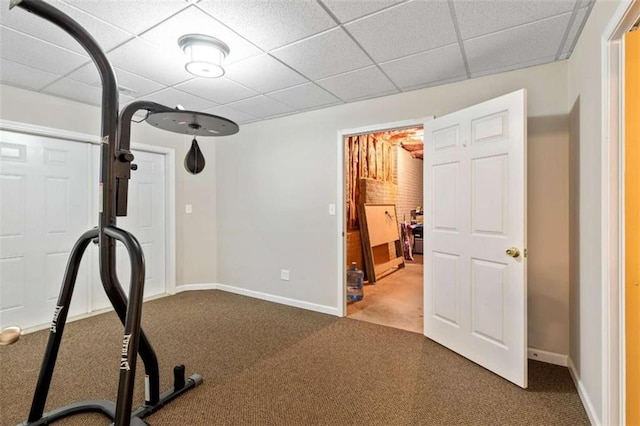 exercise room featuring baseboards, a paneled ceiling, and carpet