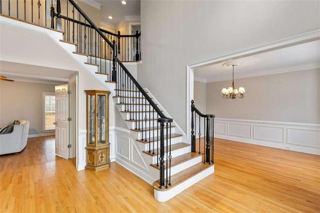 stairway with ornamental molding, wood finished floors, recessed lighting, wainscoting, and a towering ceiling