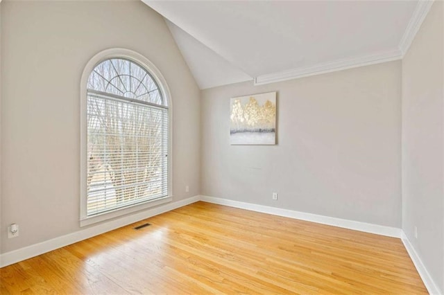 spare room featuring wood finished floors, visible vents, baseboards, ornamental molding, and vaulted ceiling