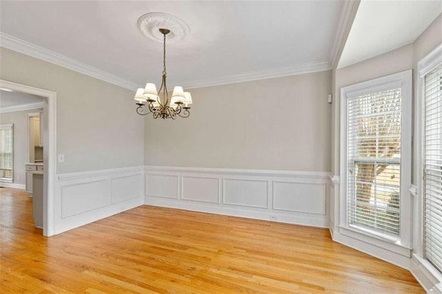 unfurnished room featuring a wainscoted wall, an inviting chandelier, ornamental molding, and light wood finished floors