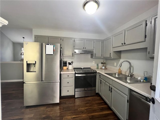 kitchen with appliances with stainless steel finishes, light countertops, gray cabinetry, under cabinet range hood, and a sink