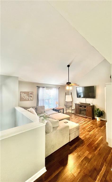 living area with a ceiling fan, vaulted ceiling, and wood finished floors