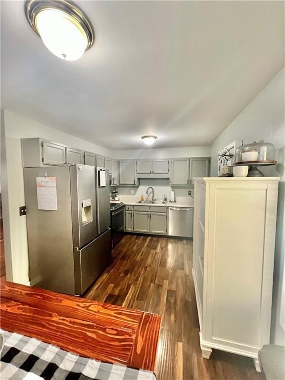 kitchen featuring appliances with stainless steel finishes, dark wood-type flooring, gray cabinets, light countertops, and a sink