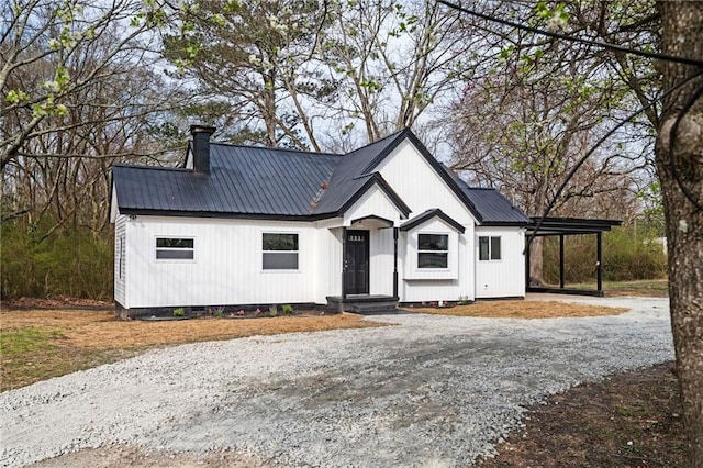 modern farmhouse featuring an attached carport, a chimney, driveway, and metal roof