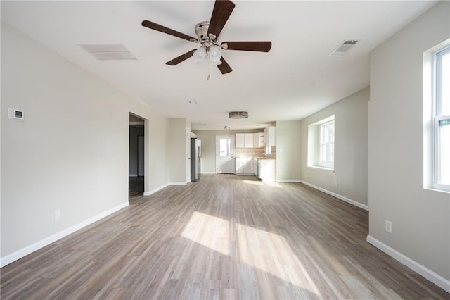 unfurnished living room with visible vents, wood finished floors, baseboards, and ceiling fan