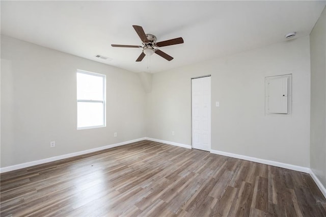 unfurnished room with visible vents, a ceiling fan, electric panel, wood finished floors, and baseboards