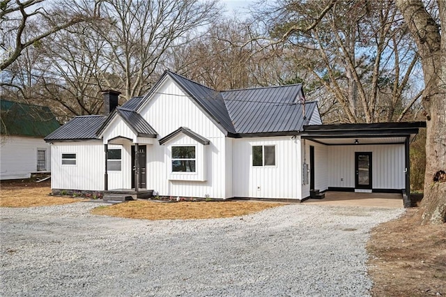 modern farmhouse featuring board and batten siding, gravel driveway, a chimney, metal roof, and a carport