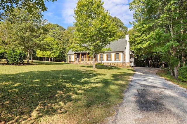 new england style home with driveway, a chimney, and a front yard