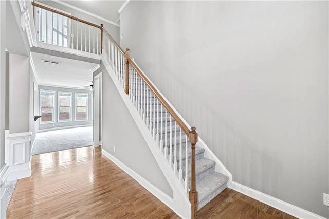 stairway featuring a high ceiling, wood finished floors, a ceiling fan, baseboards, and ornamental molding