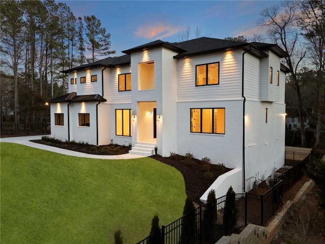 view of front of home with entry steps, brick siding, fence, and a yard