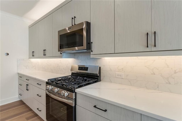 kitchen featuring light wood-style floors, appliances with stainless steel finishes, backsplash, light stone countertops, and crown molding