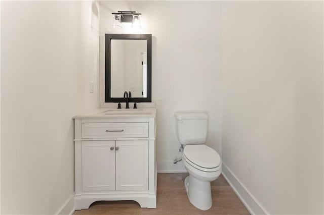 half bathroom featuring toilet, baseboards, wood finished floors, and vanity