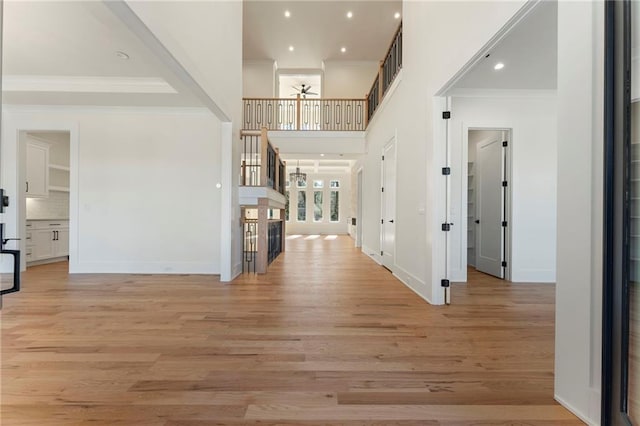 foyer entrance featuring baseboards, stairway, light wood-style flooring, and crown molding