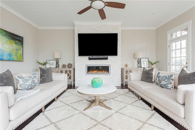 living area featuring a ceiling fan, a fireplace, crown molding, and wood finished floors