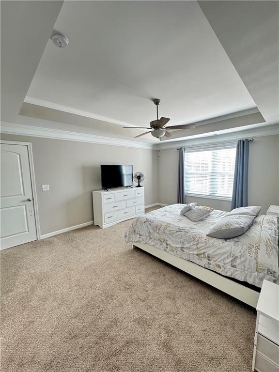 bedroom featuring carpet floors, ornamental molding, a raised ceiling, and baseboards