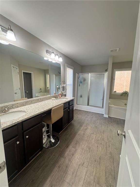 full bathroom featuring a garden tub, double vanity, a stall shower, a sink, and wood finished floors