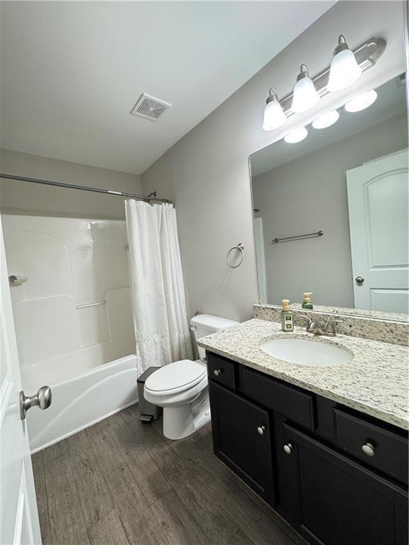 bathroom with shower / tub combo, visible vents, toilet, wood finished floors, and vanity