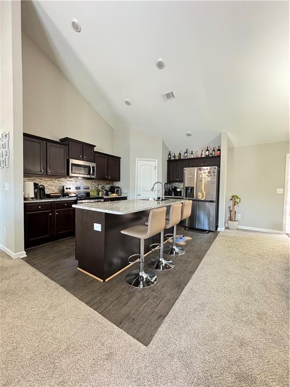 kitchen with visible vents, an island with sink, appliances with stainless steel finishes, a breakfast bar area, and dark carpet