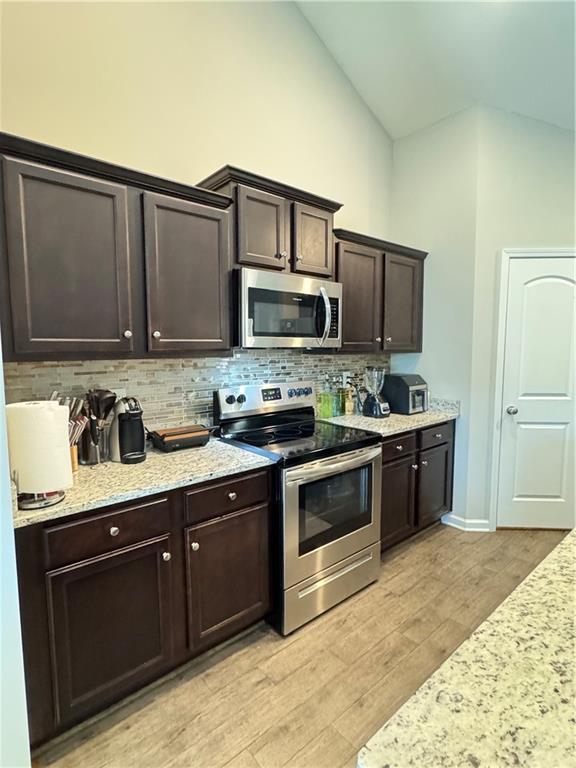 kitchen with decorative backsplash, light wood-style flooring, appliances with stainless steel finishes, light stone countertops, and dark brown cabinets