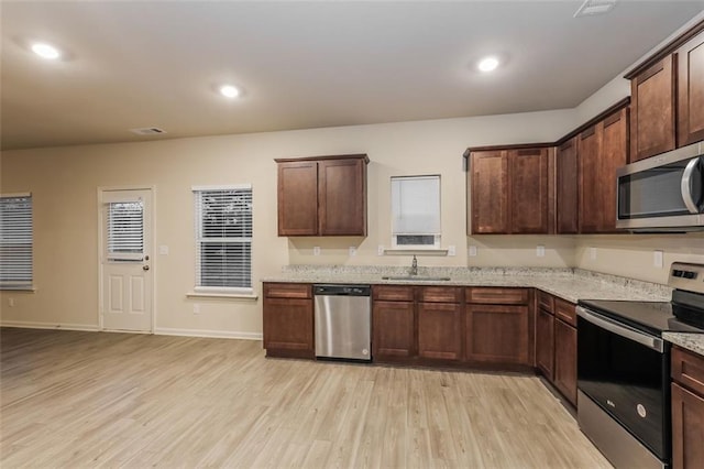 kitchen with sink, appliances with stainless steel finishes, light stone counters, dark brown cabinetry, and light hardwood / wood-style floors