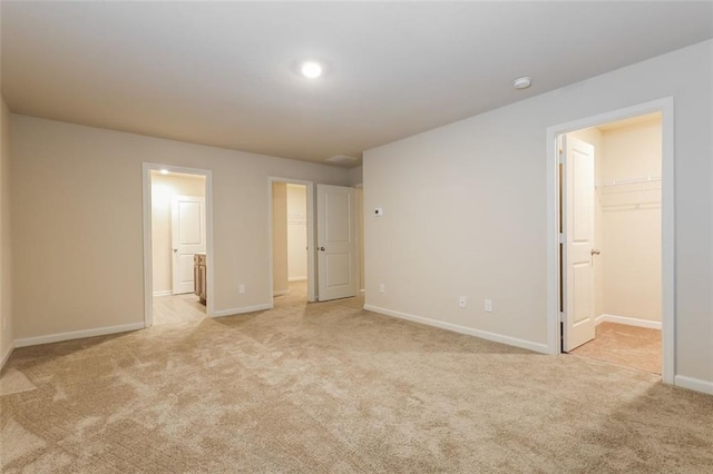 unfurnished bedroom featuring a walk in closet, a closet, and light carpet