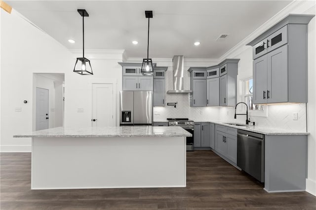 kitchen with a sink, appliances with stainless steel finishes, a center island, wall chimney exhaust hood, and pendant lighting