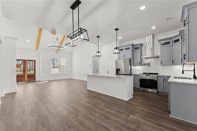 kitchen with pendant lighting, appliances with stainless steel finishes, a sink, a kitchen island, and wall chimney exhaust hood