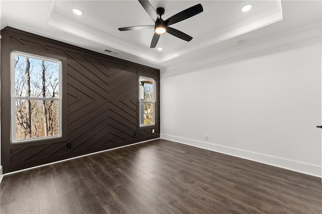 empty room featuring a tray ceiling, dark wood-style flooring, plenty of natural light, and baseboards