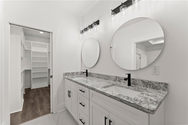 bathroom featuring a walk in closet, a sink, baseboards, and double vanity