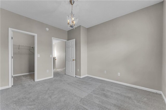 unfurnished bedroom with a chandelier, a walk in closet, light colored carpet, and a closet