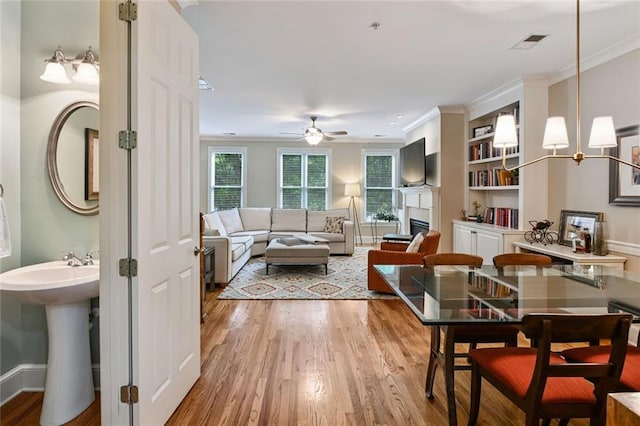 living area featuring ornamental molding, a ceiling fan, light wood-style flooring, and visible vents