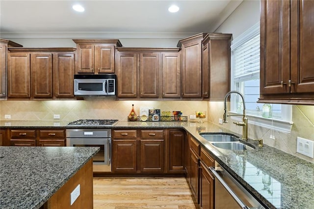 kitchen with a sink, appliances with stainless steel finishes, light wood finished floors, and dark stone countertops