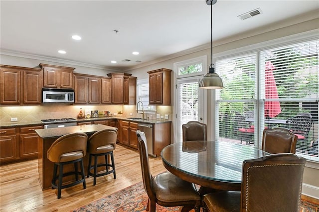 kitchen featuring visible vents, ornamental molding, a kitchen island, a sink, and stainless steel appliances