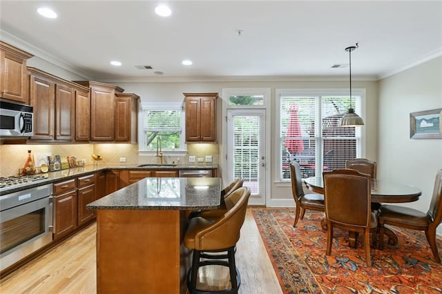 kitchen featuring a kitchen island, crown molding, appliances with stainless steel finishes, a sink, and light wood-style flooring