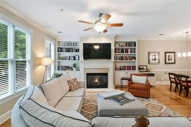 living room with crown molding, a fireplace with flush hearth, wood finished floors, and ceiling fan with notable chandelier