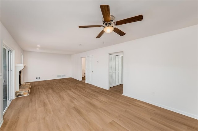 unfurnished living room with visible vents, a fireplace with raised hearth, light wood-style flooring, and baseboards