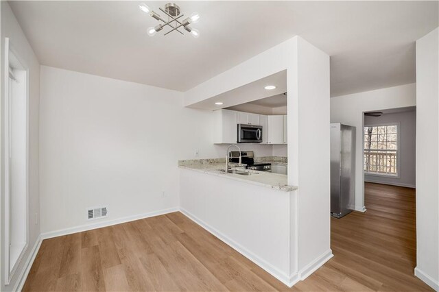 kitchen with visible vents, stainless steel appliances, light wood-type flooring, white cabinetry, and a sink