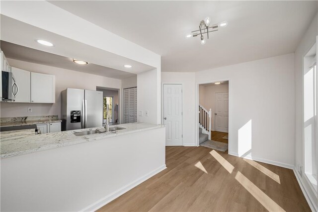 kitchen featuring stainless steel appliances, light wood-style flooring, white cabinetry, light stone countertops, and baseboards